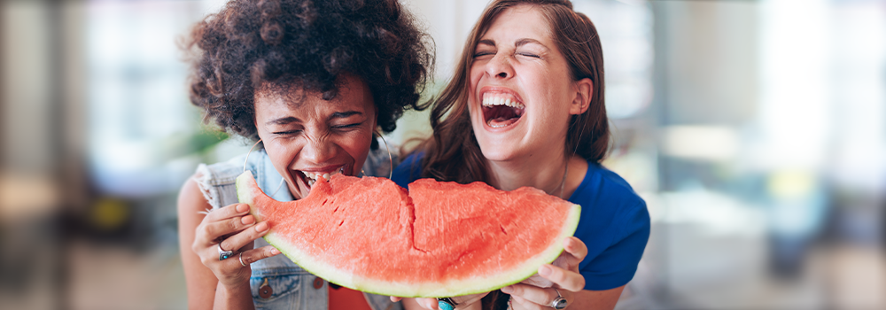 Die smarte Budgetierung: Zwei junge Frauen teilen sich ein Stück Wassermelone und haben viel Spaß dabei