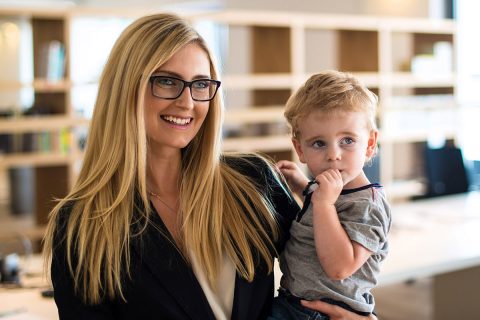 volksbank mittelhessen zukunftplanerin Mutter in Geschäftskleidung trägt stolz einen kleinen Jungen auf dem Arm in Büroumgebung